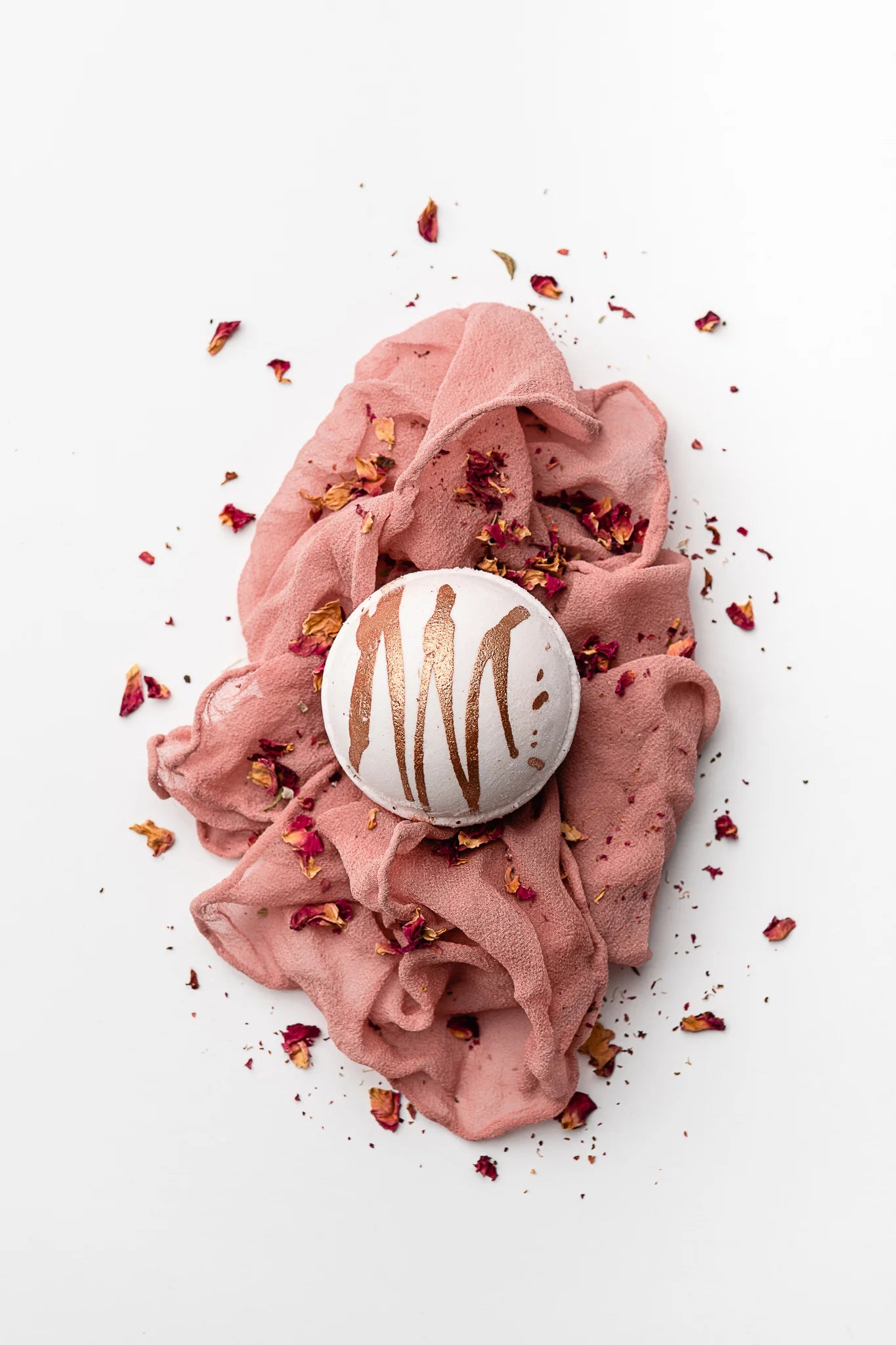 white bath bomb with a copper drizzle on a pink muslin cloth