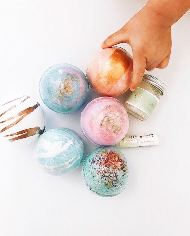 Colorful bath bombs with a hand reaching for one on a white surface.