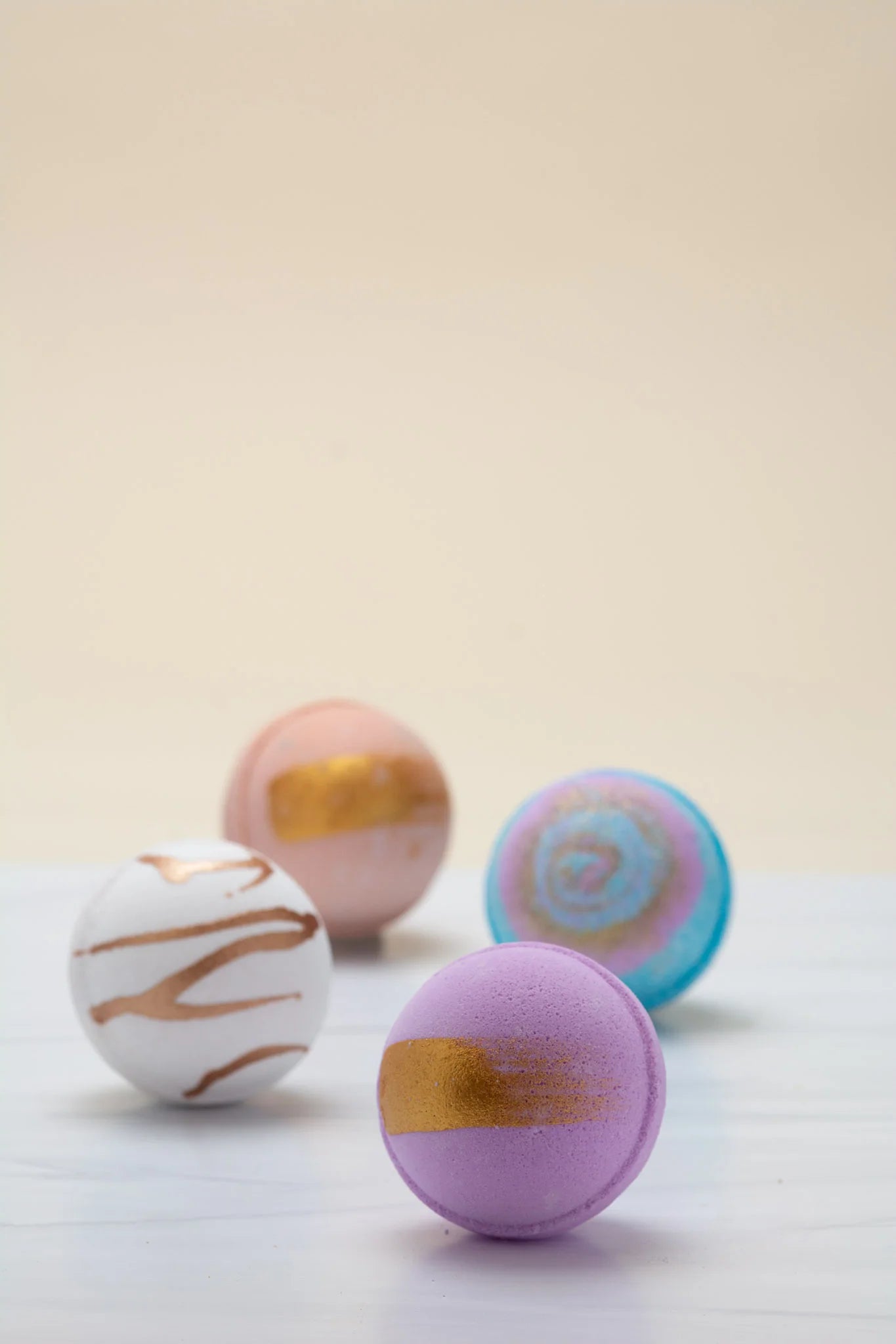 Four bath bombs with gold and blue designs on a light background