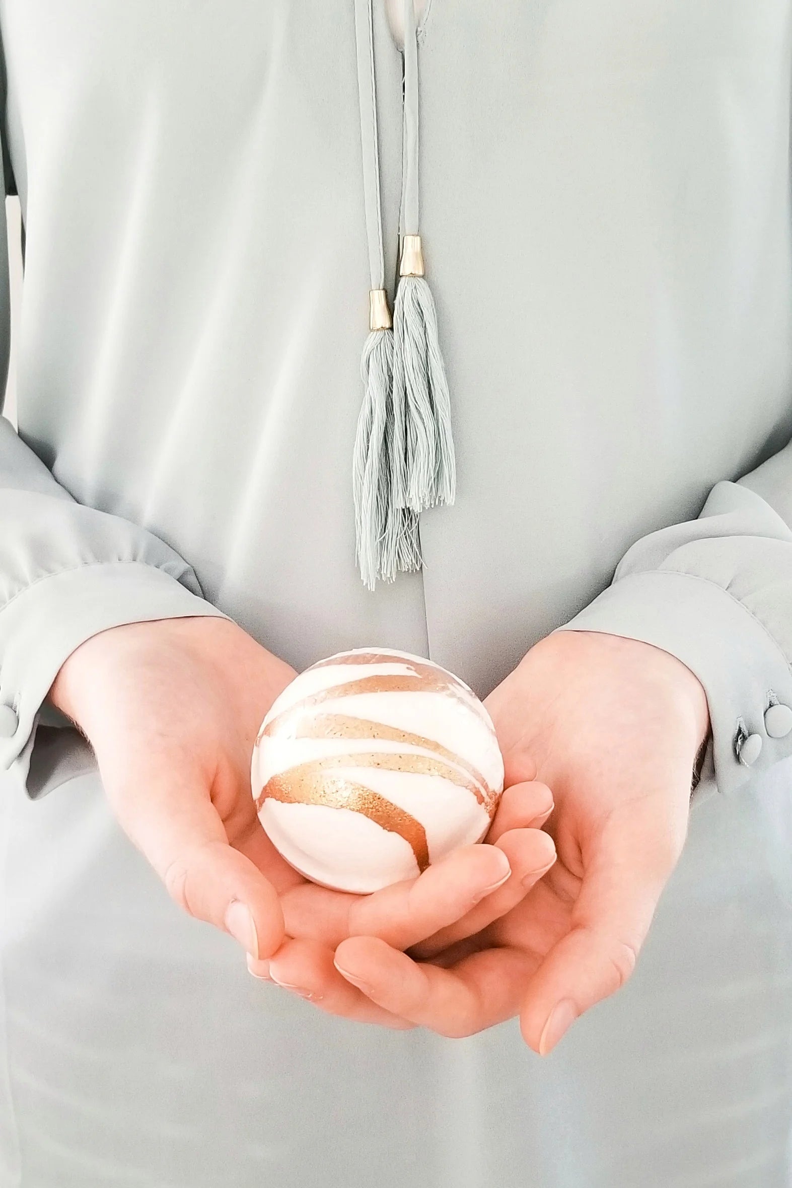Person holding a bath bomb sphere in their hands against a neutral background