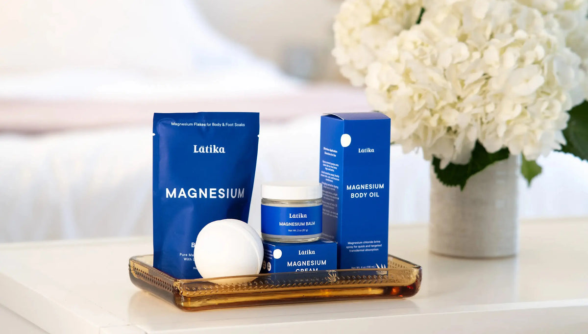 Latika magnesium products including a bag, jar, and bottle on a tray with white flowers in the background.