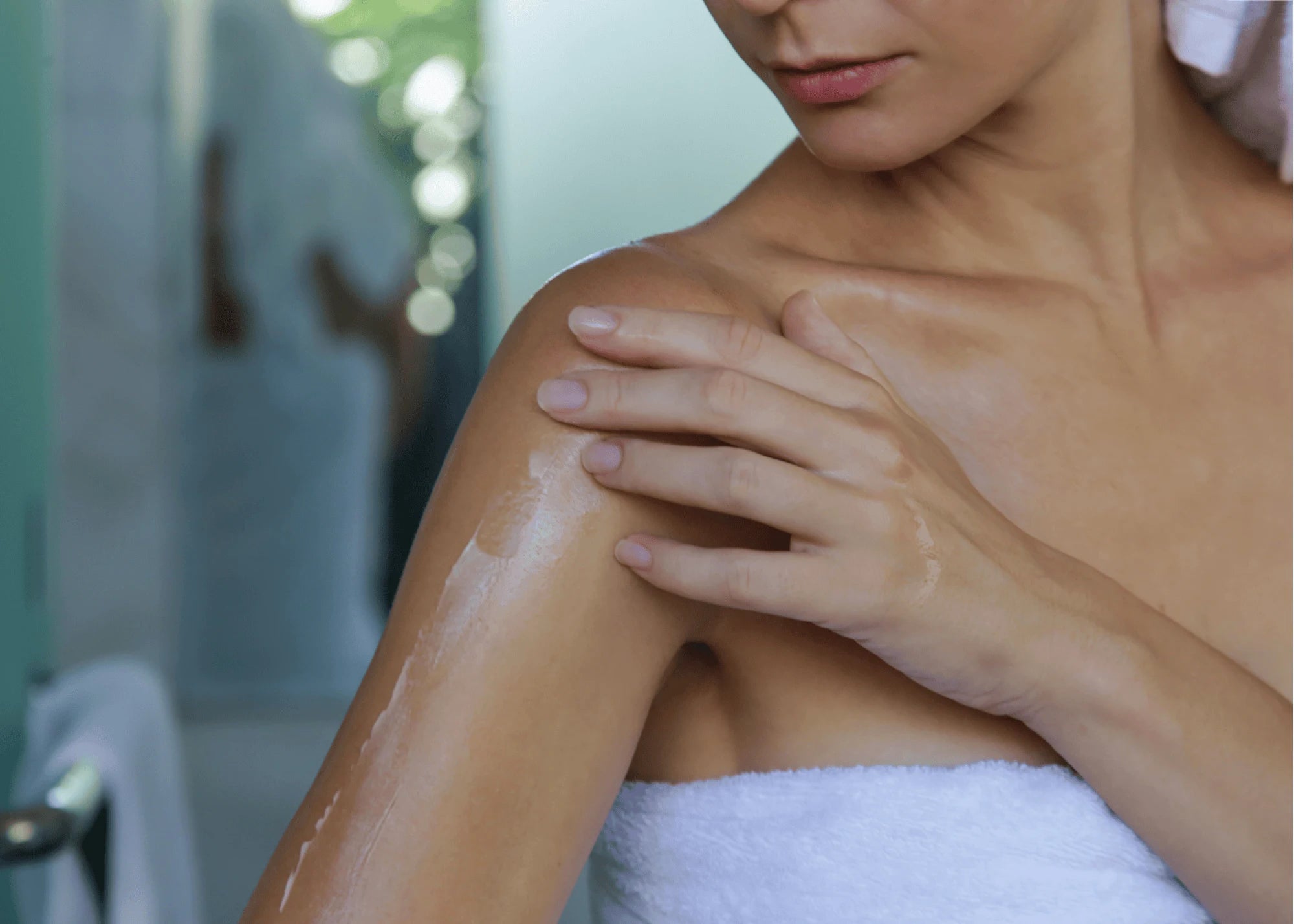 Person applying sunscreen to their shoulder with a towel around their neck.