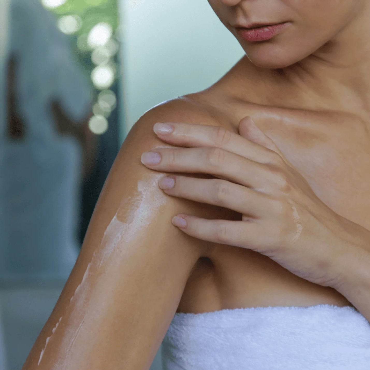 Person applying sunscreen to their shoulder with a towel around their neck.