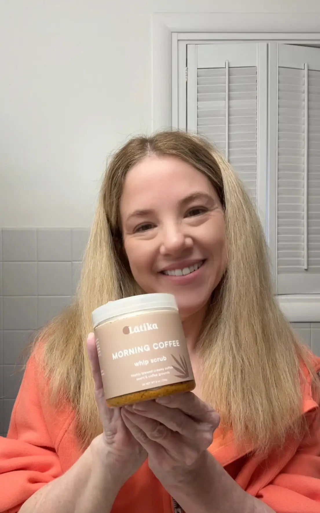 Person holding a jar of 'Morning Coffee' candle in a bathroom.