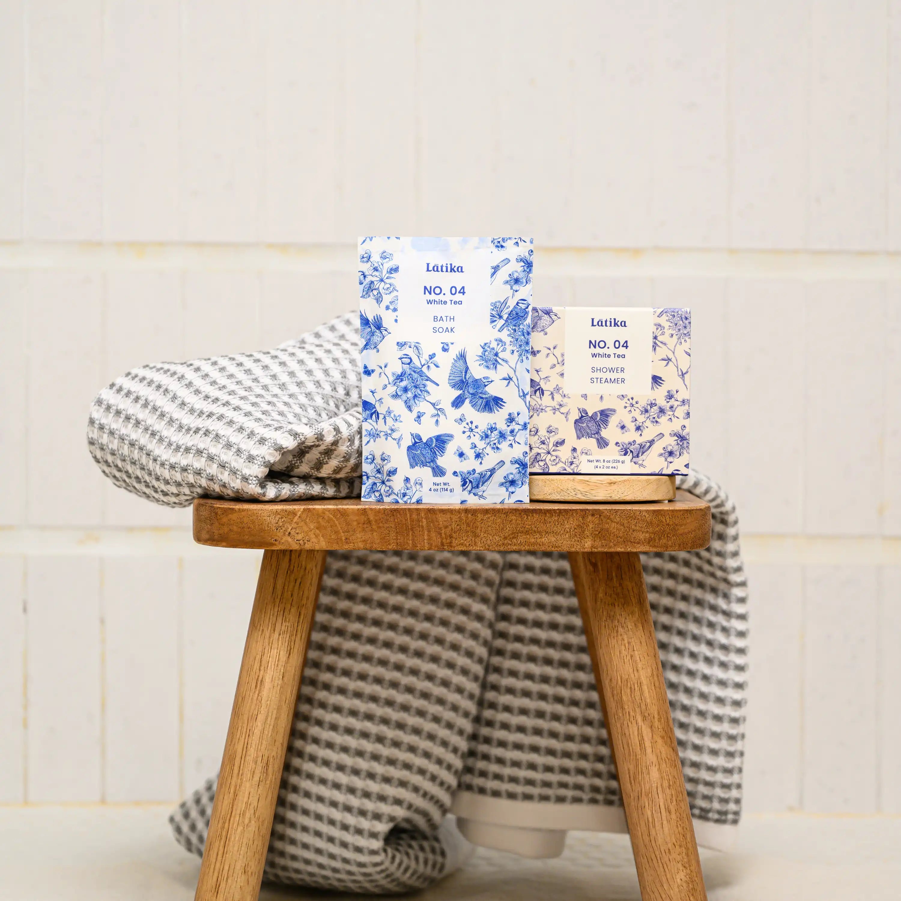 Latika milk bath soak in white tea and whiite tea shower steamers on a bath stool