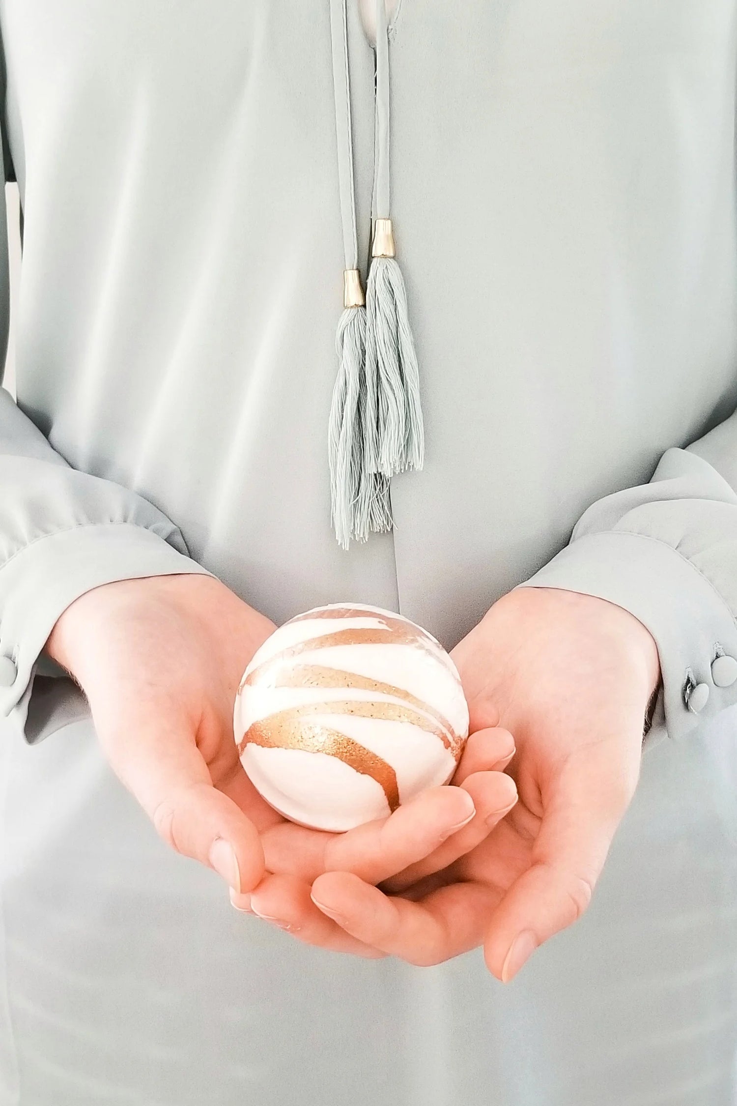 Person holding a bath bomb sphere in their hands against a neutral background