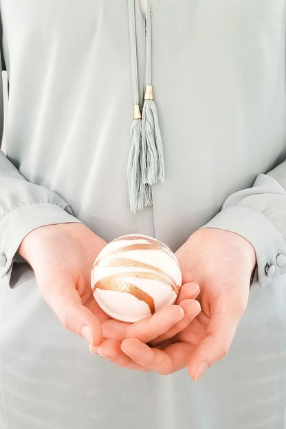 Person holding a bath bomb sphere in their hands against a neutral background