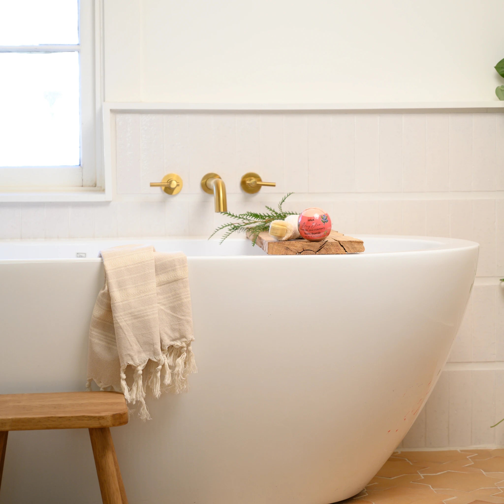 White freestanding bathtub with a wooden stool and decorative items in a bathroom.