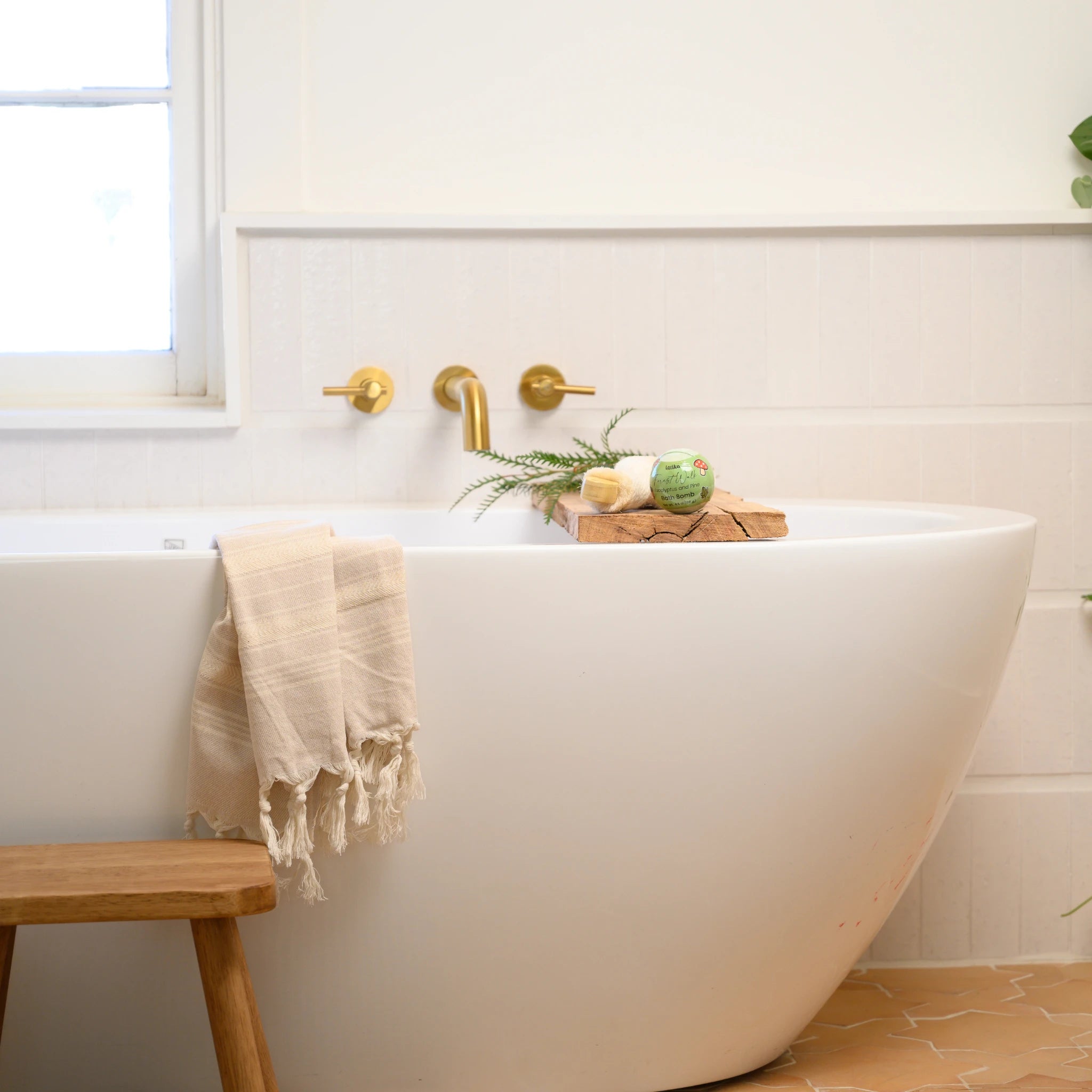 White freestanding bathtub with a wooden stool and decorative items in a bathroom.
