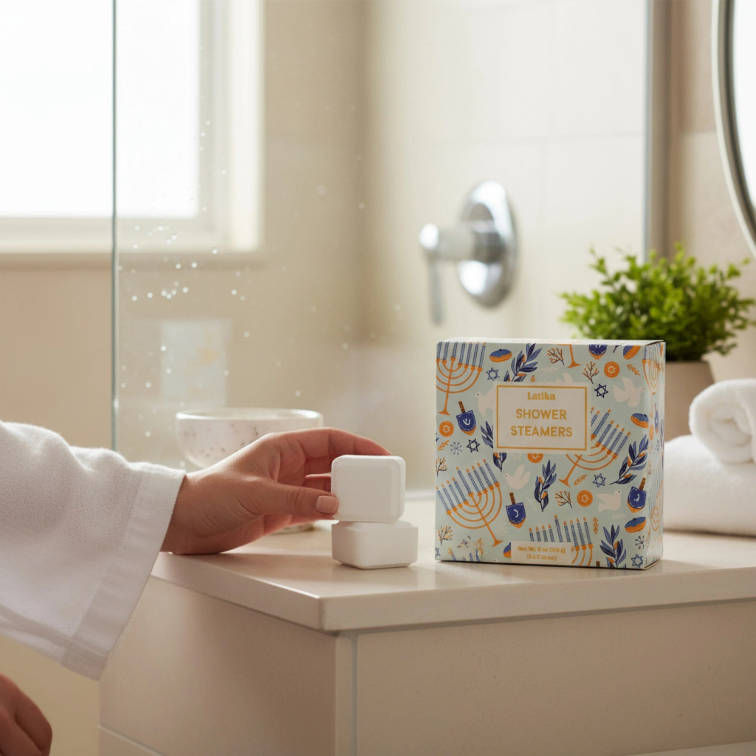 Person holding a shower steamer next to a box of Hanukkah shower steamers in a bathroom setting.