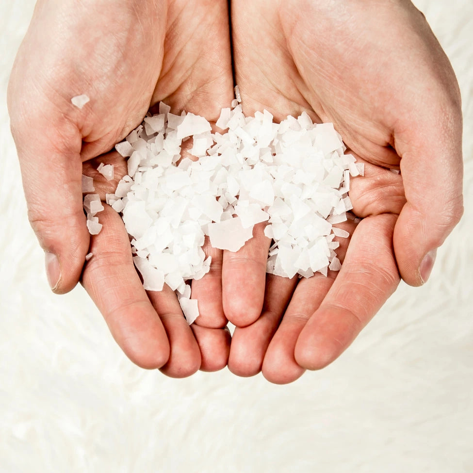 Two hands holding a small pile of white salt crystals against a light background
