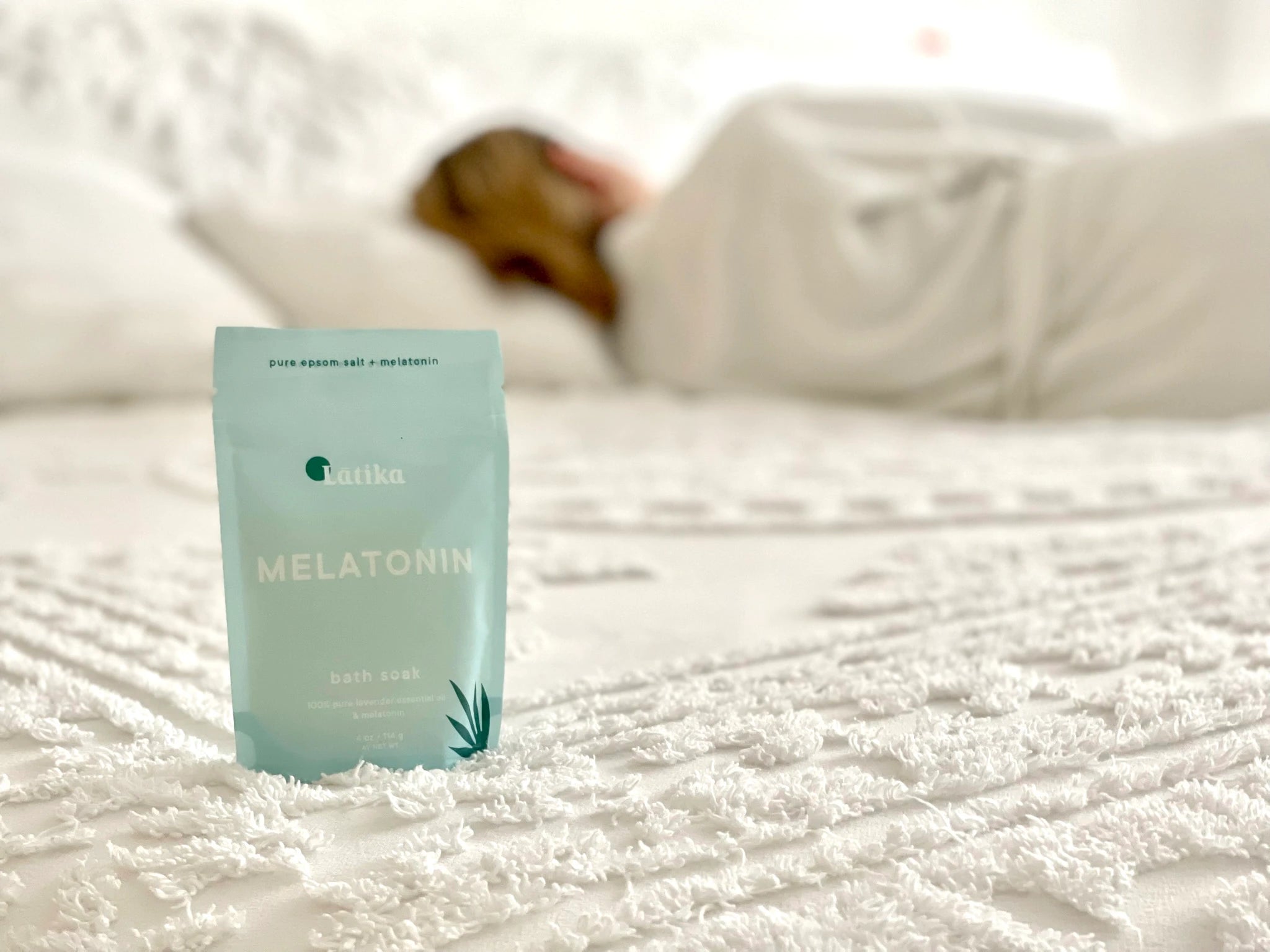 Melatonin package on a bed with a blurred person asleep in the background