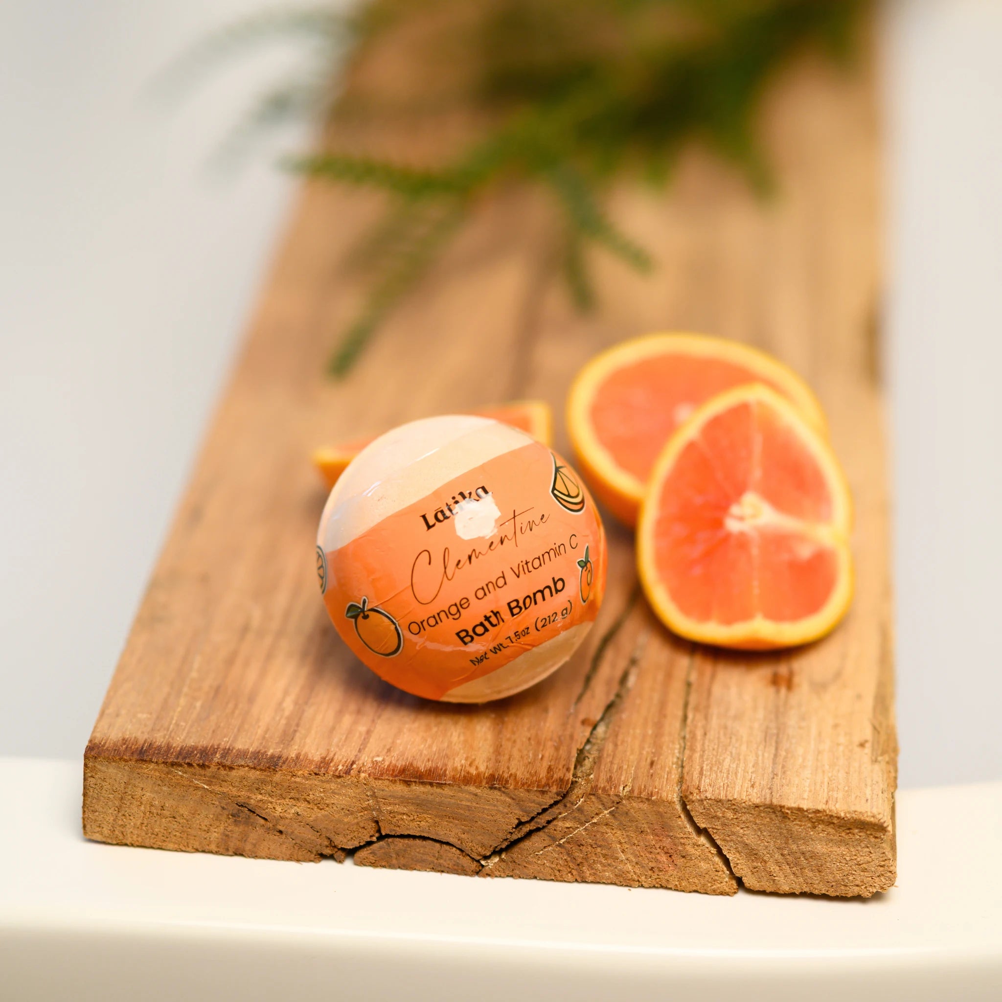 Bath bomb with orange and vitamin C packaging on a wooden board with sliced oranges.