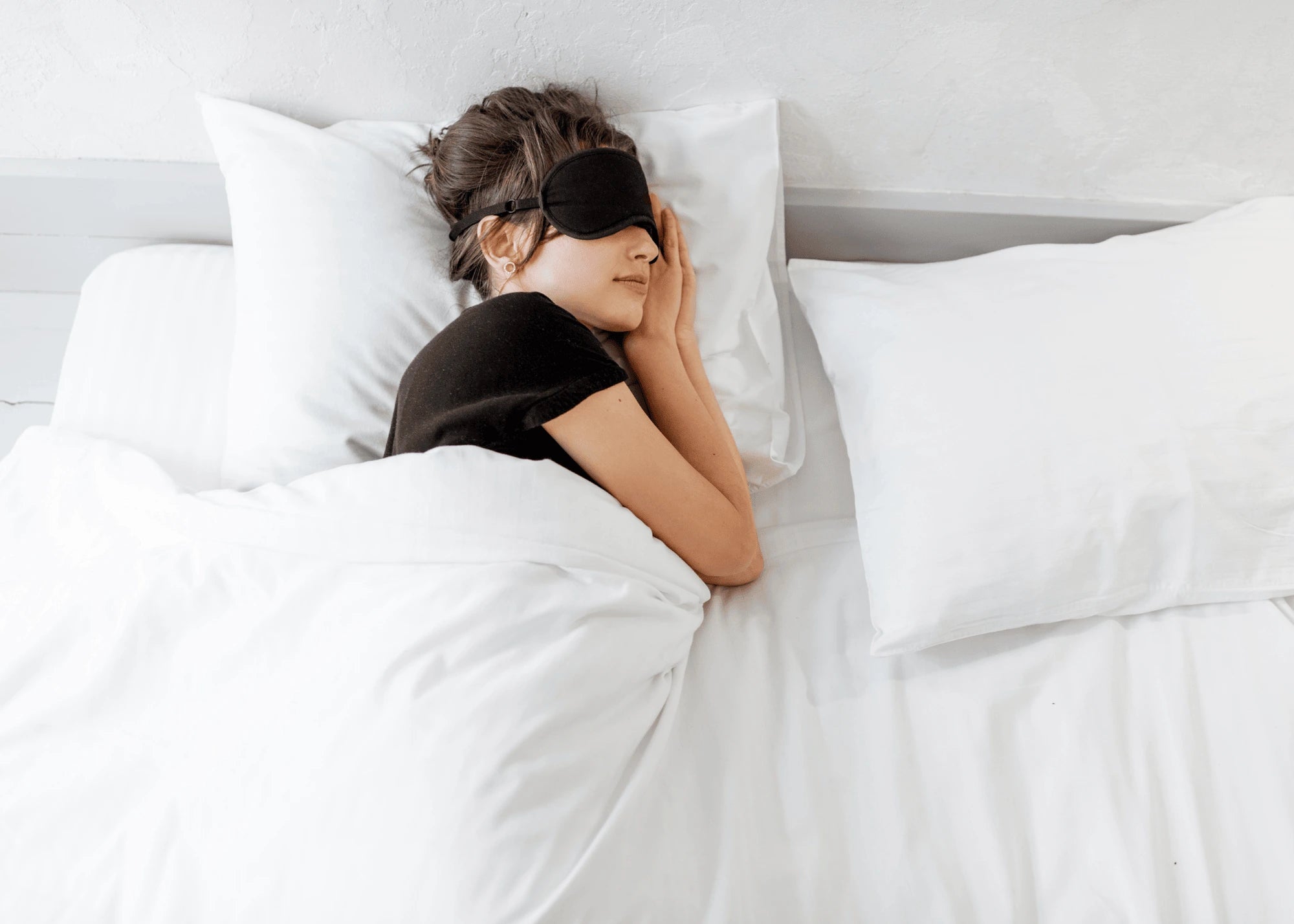 Person sleeping in bed with a black sleep mask on, wearing a black shirt.