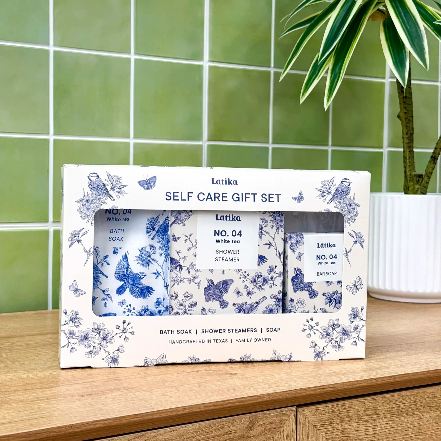 Latika self-care gift set with bath soap, shower steamer, and bar soap on a wooden surface with green tiled wall in the background.