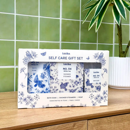Latika self-care gift set with bath soap, shower steamer, and bar soap on a wooden surface with green tiled wall in the background.