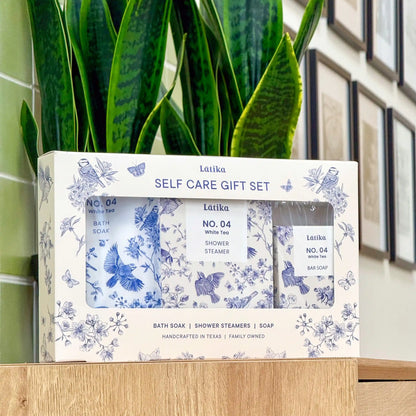 Latika self-care gift set with bath soap, shower steamer, and soap in front of a green plant. chinoiserie pattern box.