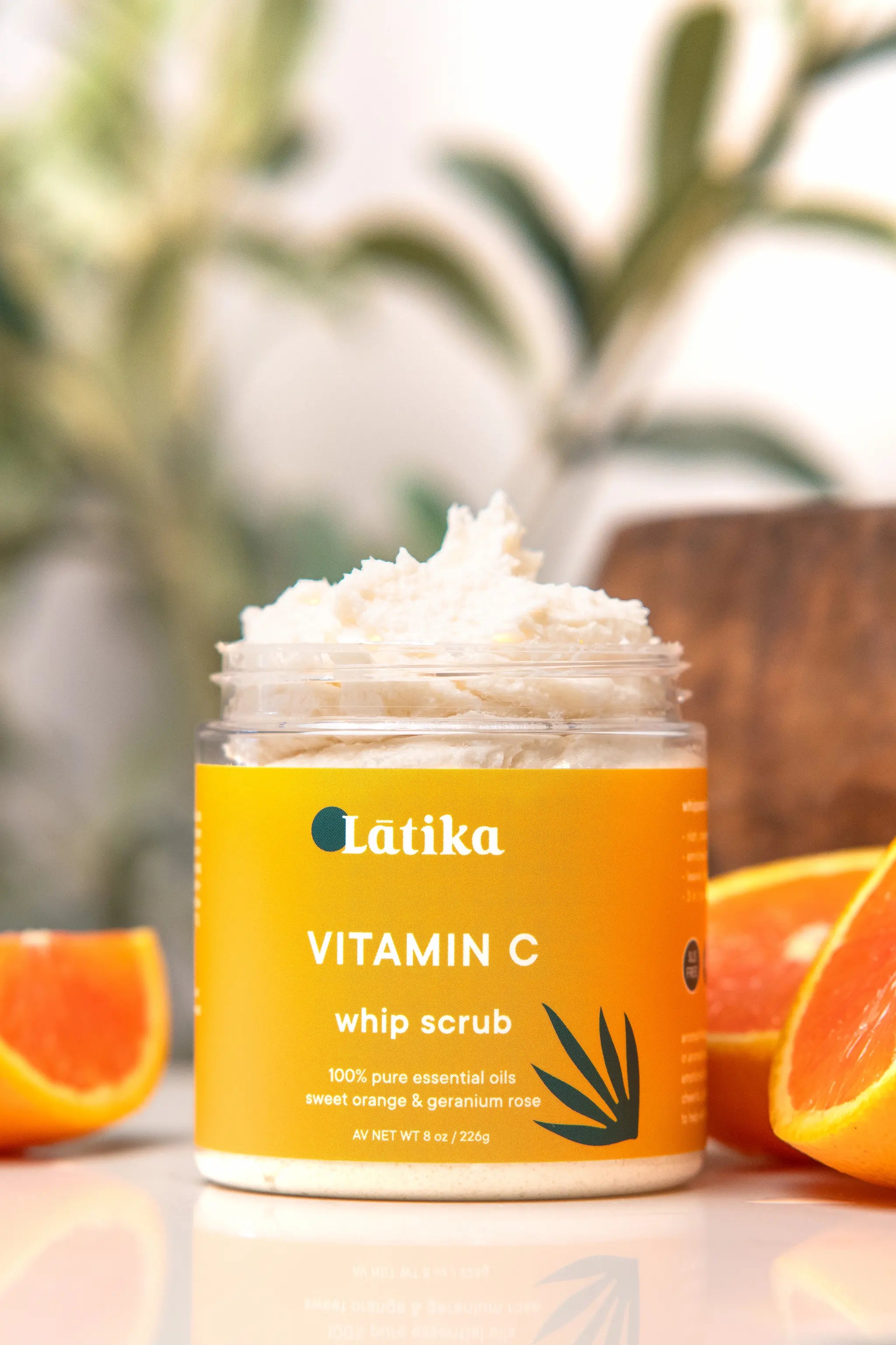 Jar of Latika Vitamin C whip scrub with oranges and a blurred natural background