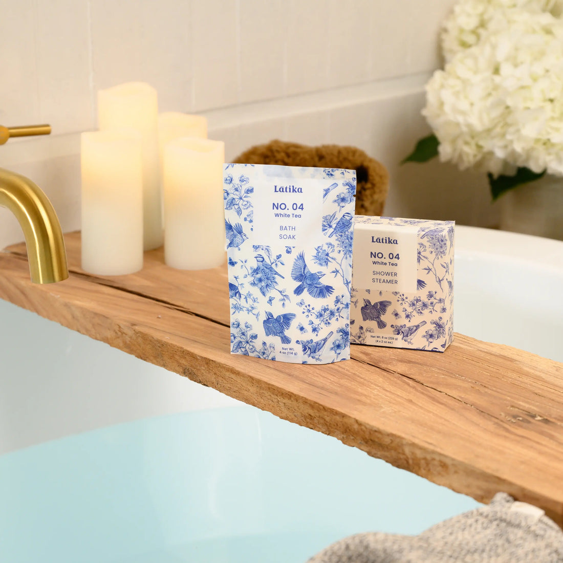 Two chinoiserie pattern soap bars on a bath tray with candles and flowers in the background.